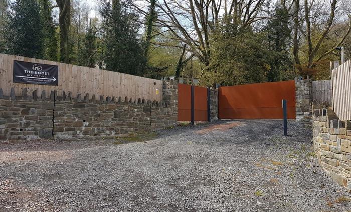 a gravel drive way with stone walls and fence on both signs. There are two gates with an intercom and a sign for the roost.